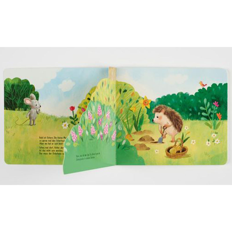 Buchseite: Klappseite geöffnet – hinter dem Busch kommt ein Igel mit Schaufel und Korb zum Vorschein, der im Gras gräbt.