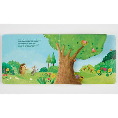 Buchseite: Maus und Igel spazieren über eine Frühlingswiese zu einem großen Baum mit Vogelnest und bunten Blumen.