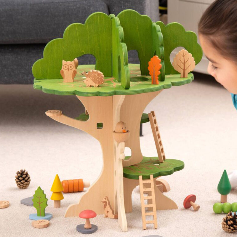 Kind spielt mit einem Holzspiel-Baum mit grüner Baumkrone, Holzleitern und kleinen Tierfiguren wie Eule und Igel.
