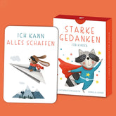 Kartenbox Starke Gedanken für Kinder mit orangefarbenem Hintergrund, illustriertem Waschbären im Superheldenkostüm und einer Beispielkarte mit Hund auf Papierflieger und der Affirmation Ich kann alles schaffen