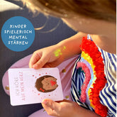 Kind hält eine Affirmationskarte mit Igelillustration und der Botschaft Ich höre auf mein Herz, farbenfrohe Kleidung und weiches Licht im Alltagsszenario