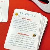 Detailaufnahme der Anleitungskarte mit Text zur täglichen Routine und Gesprächsimpulsen, Kartenstapel auf rotem Hintergrund