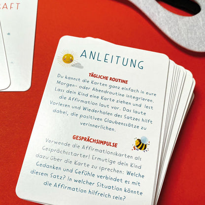 Detailaufnahme der Anleitungskarte mit Text zur täglichen Routine und Gesprächsimpulsen, Kartenstapel auf rotem Hintergrund