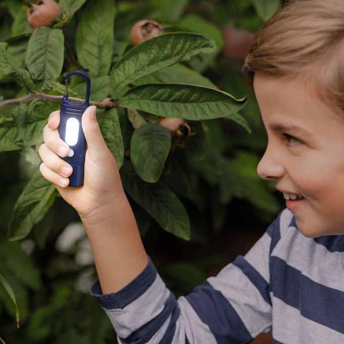 Kind leuchtet mit blauer Clip Taschenlampe in der Natur