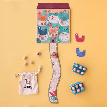 Aufgebautes Spiel „Cluck, cluck! the fox!“ mit Spielfeld, bunten Hühnern, Eiern und Zubehörteilen auf gelbem Hintergrund.