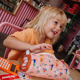 Kind sitzt am Tisch mit Taschenrechner und Federmappe in der Farbe Flore vor sich am Tisch