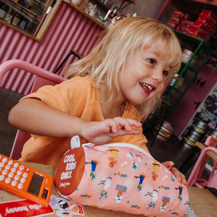 Kind sitzt am Tisch mit Taschenrechner und Federmappe in der Farbe Flore vor sich am Tisch