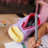 Kind hält Farbstift während im Hintergrund geöffnete Federmappe in der Farbe Mini Mauve liegt