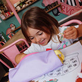 Kind sitzt am Tisch mit Button in der linken Hand während die rechte Hand in der Federmappe stöbert