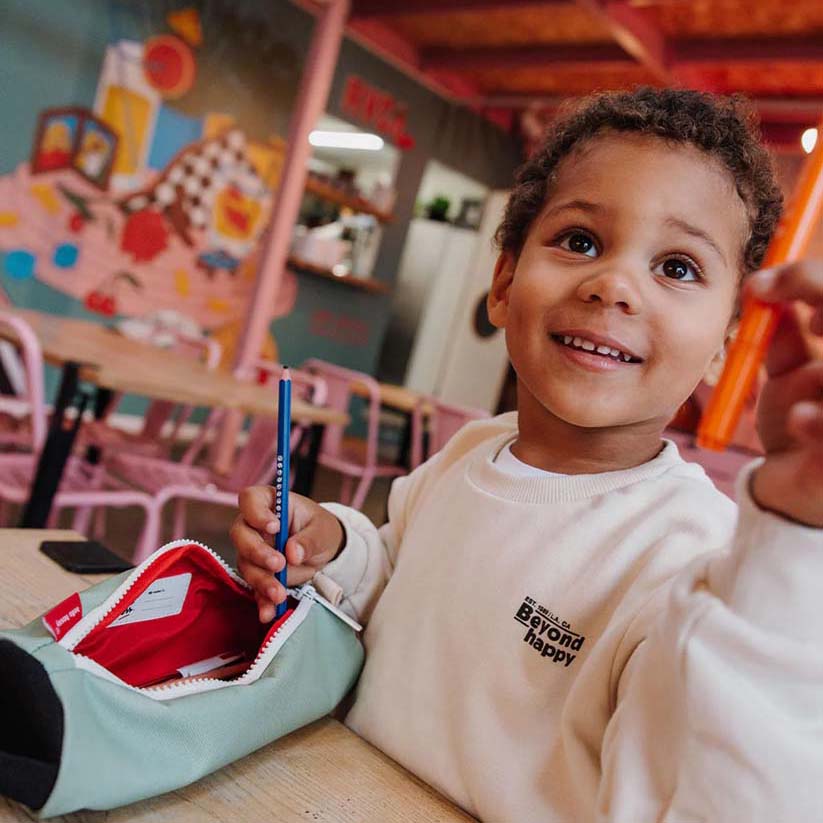 Kind hält Stift in die Kamera während Federmappe in der Farbe Mini Pistache am Tisch liegt