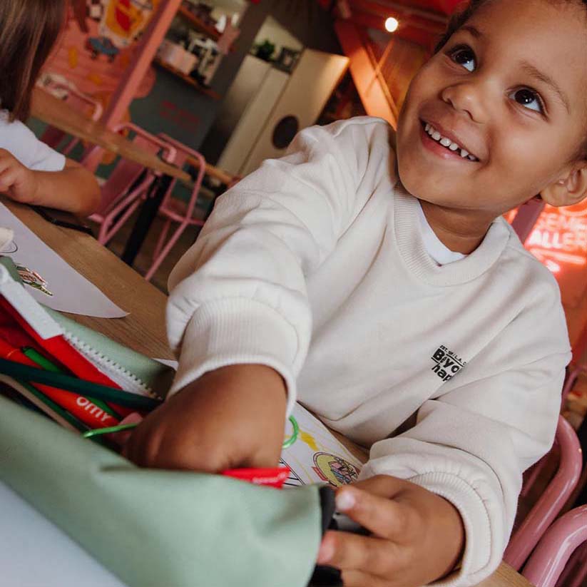 Kind schaut links an der Kamera vorbei während es Stifte auf der Federmappe holt