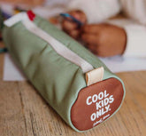 Geschlossene Federmappe in der Farbe Mini Pistache liegt am Tisch mit Kinderhänden im Hintergrund