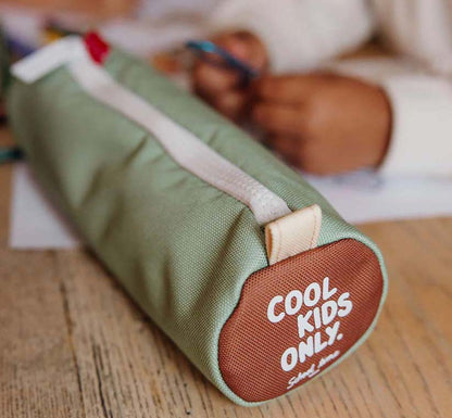 Geschlossene Federmappe in der Farbe Mini Pistache liegt am Tisch mit Kinderhänden im Hintergrund