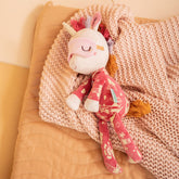 Plüsch-Einhorn mit Schlafmaske liegt gemütlich auf einer rosa Decke.
