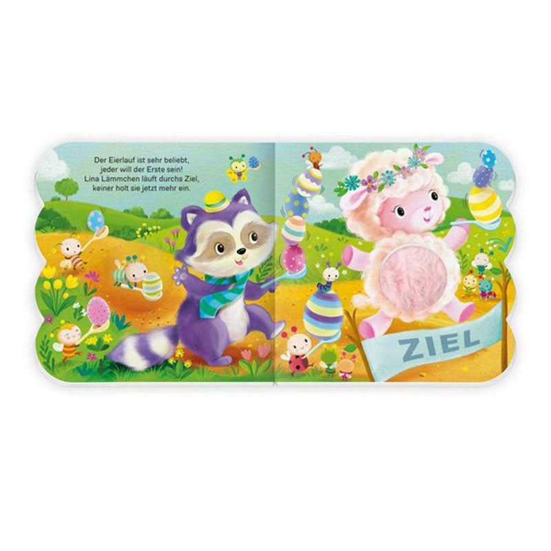 Buchseite mit Osterspielszene auf einer Frühlingswiese, einem Waschbären, einem springenden Lamm mit rosa Fühlelement, bunten Ostereiern, Blumen und dem Ziel-Schild in kindgerechter Illustration
