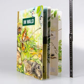 Buch „Im Wald“ aufrecht stehend mit Lineal daneben zur Größenansicht.