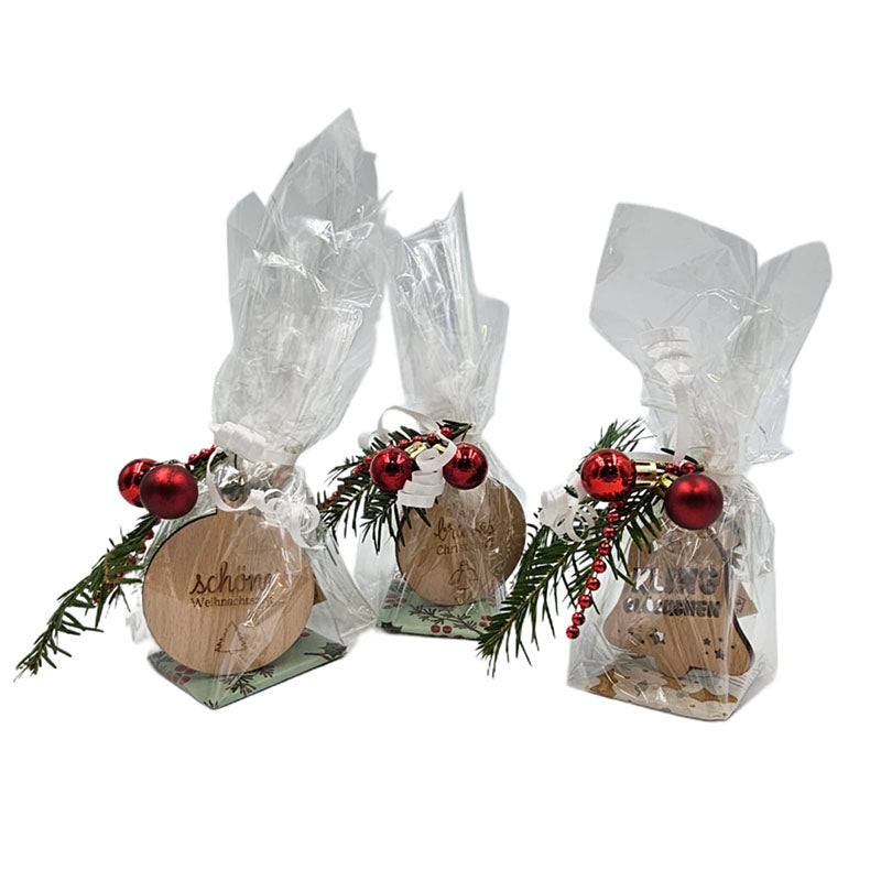 Drei weihnachtlich verpackte Geschenksets mit Holzanhängern, Tannenzweigen und roten Kugeln.