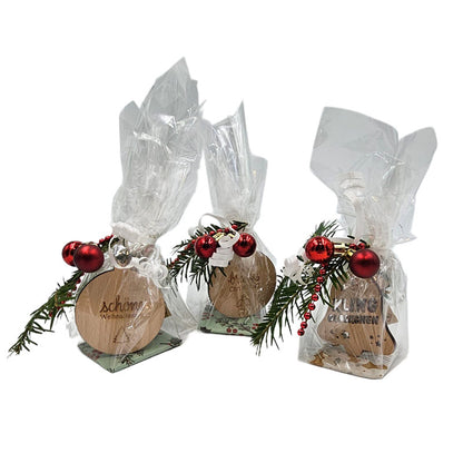 Drei weihnachtlich verpackte Geschenksets mit Holzanhängern, Tannenzweigen und roten Kugeln.
