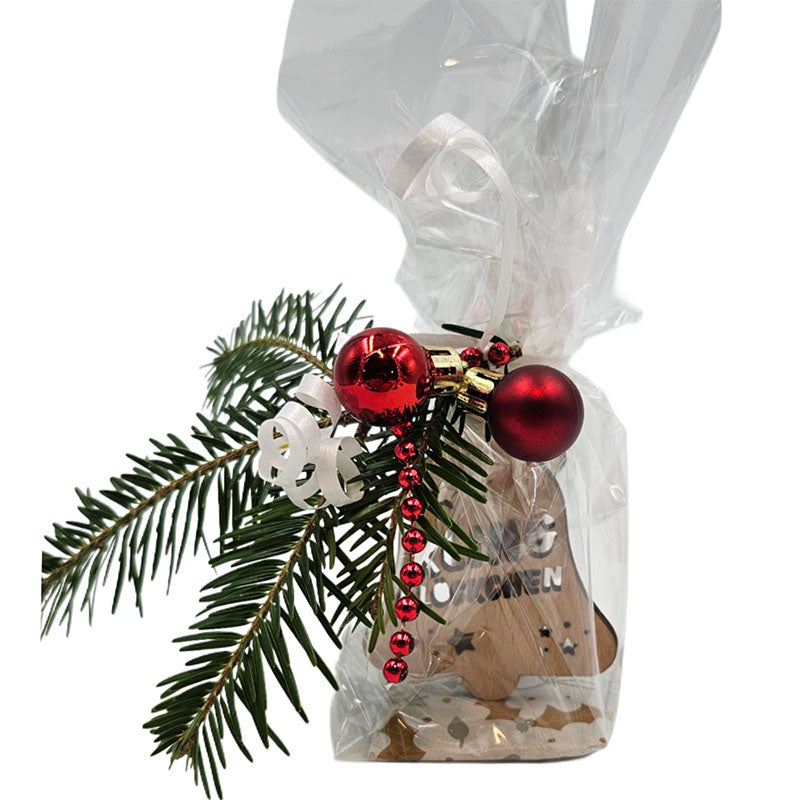 Nahaufnahme eines Geschenksets im Zellophan, dekoriert mit Tannenzweig, roten Kugeln und Holzanhänger in Glockenform