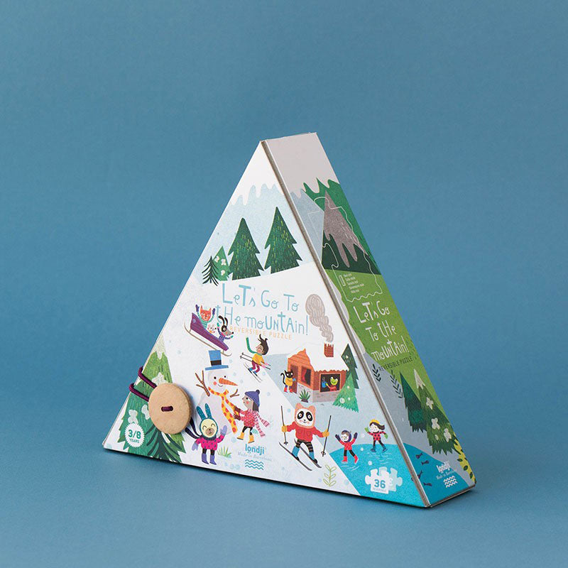 Rückseite der Pyramidenverpackung des Puzzles mit winterlicher Illustration: Kinder beim Skifahren, Rodeln und Schneemannbauen, beschriftet mit „Let’s Go to the Mountain!“.
