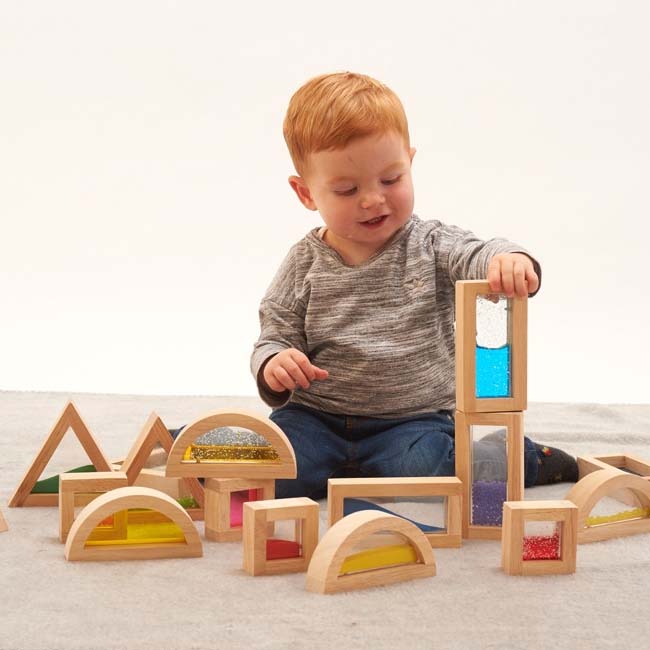 Kleinkind sitzt inmitten sensorischer Bausteine und baut einen Turm aus zwei länglichen Bausteinen