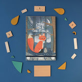 Produktfoto mit der Verpackung des Holzspiels in der Mitte, umgeben von den verschiedenen farbigen Holzformen auf blauem Hintergrund.