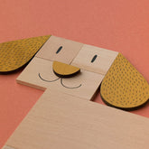 Nahaufnahme eines aus Holzteilen gelegten Hundegesichts mit braunen Ohren auf orangem Hintergrund.