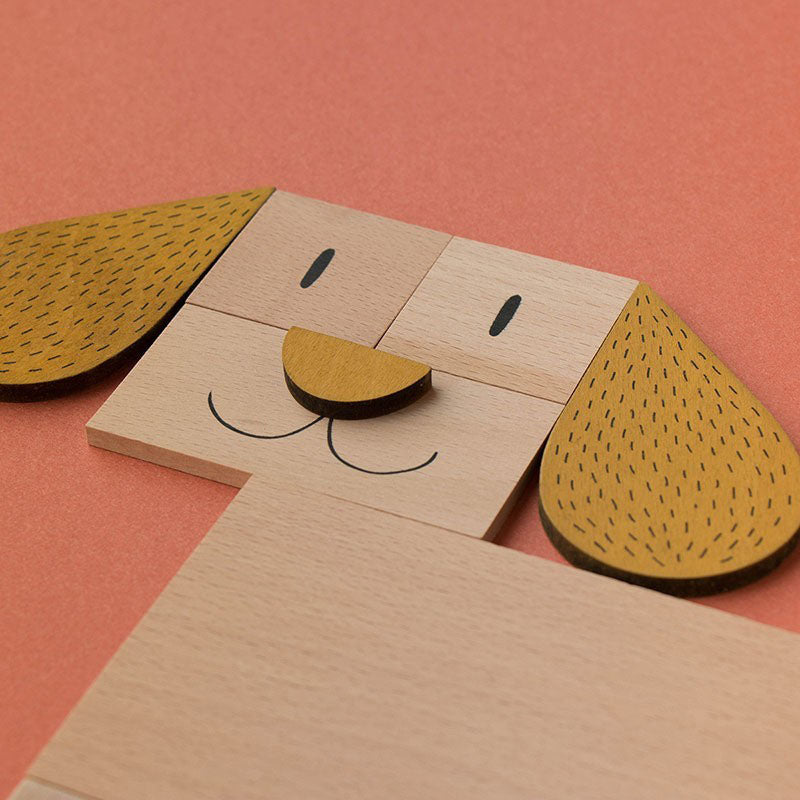 Nahaufnahme eines aus Holzteilen gelegten Hundegesichts mit braunen Ohren auf orangem Hintergrund.