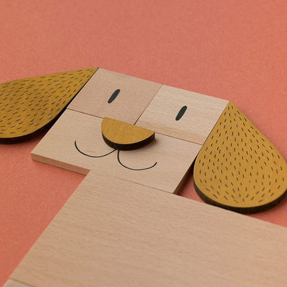 Nahaufnahme eines aus Holzteilen gelegten Hundegesichts mit braunen Ohren auf orangem Hintergrund.