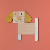 Komplettes Hundemotiv aus Holzformen mit langen Ohren und fröhlichem Gesicht auf orangem Hintergrund.