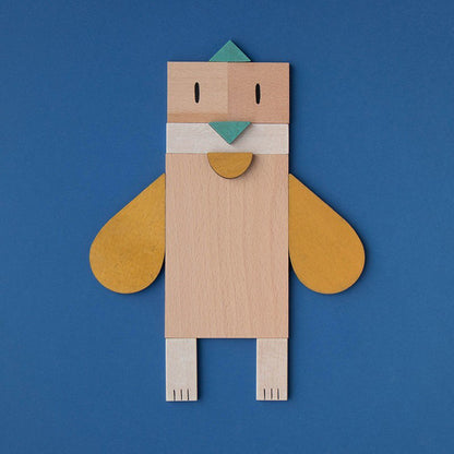 Vogel aus Holzformen mit gelben Flügeln und grünem Schnabel auf blauem Hintergrund.