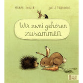 Buchcover: Hase und Igel sitzen sich gegenüber, vor ihnen liegt eine Möhre, Titel „Wir zwei gehören zusammen“ auf hellem Hintergrund.