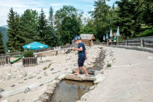 Junge balanciert am Wasserspielplatz barfuß über einen Stein uner dem ein Bächlein durchrinnt