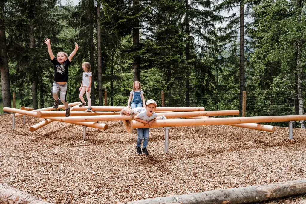 vier Kindergartenkinder beim Spielen im Waldpark auf Holzstangen