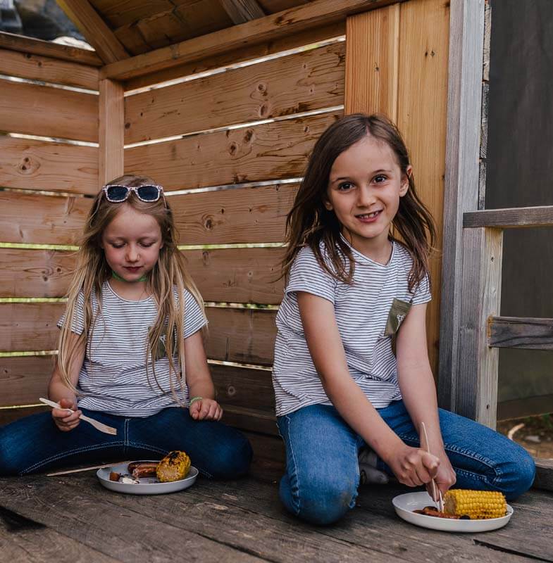 Zwei Mädchen genießen ihre gegrillten Maiskolben in einer der Picknickhütten